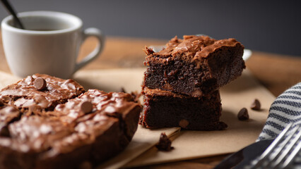 Chocolate chip brownies with coffee and chocolate chips with fork and knife on a wooden board and some baking paper. - obrazy, fototapety, plakaty