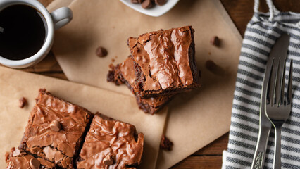 Chocolate chip brownies with coffee and chocolate chips with fork and knife on a wooden board and some baking paper.