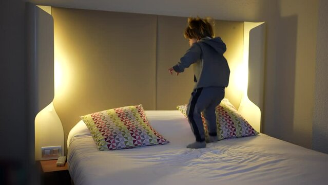 Carefree child bounding up and down in hotel bed during vacation travel