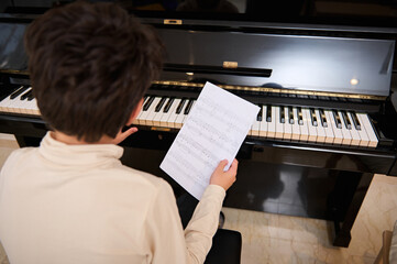 Details on musical notes on white paper sheet in the hands of a teenage boy playing grand piano...