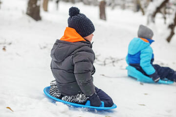 Child girl ride in snow plate. Outdoor play. Cold temperature. Winter time. Back view