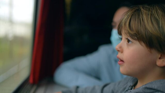 Closeup child's face traveling by train looking at scenery pass by. Happy small boy passenger daydreaming while looking at view from high speed transportation