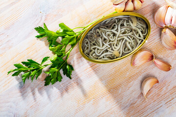 Image of pickled eels in open tin can with garlic at table, nobody