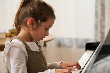 Little girl pianist plays piano and sings indoor, creates music and song, performs on the...
