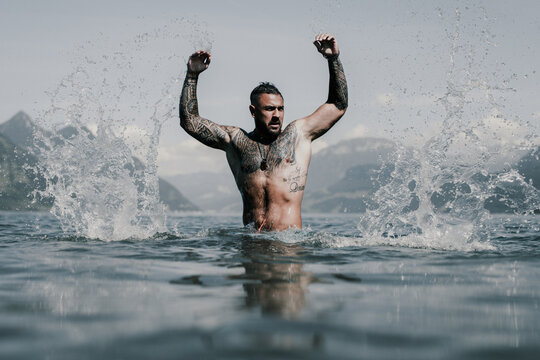 Naked muscular Hispanic man splashing water in lake. Attractive male sexy model in water. Handsome boy rest in Alps lake water. Sexy man naked torso in water. Man freedom lifestyle. Strong muscles guy