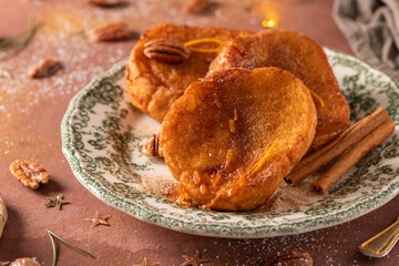 Traditional Christmas french toast or rabanadas with sugar syrup, cinnamon and pecan nuts on a rustic kitchen counter at Christmas time.