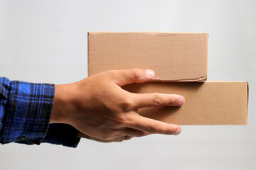 A hand holding a cardboard box against a gray background, illustrating the concept of shipping, delivery, and logistics services