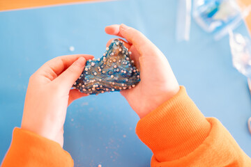 Plasticine games. Blue slime in childrens hands on a blue silicone mat on a wooden table. View from...