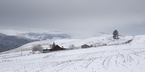 An idyllic remote farm, with its fields covered in snow, and farmhouse roof covered in snow, with a...