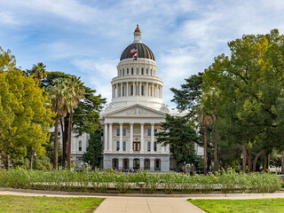 A image of the State Capitol Building in Sacramento, California on a beautiful day with a blue sky and green trees surrounding the building