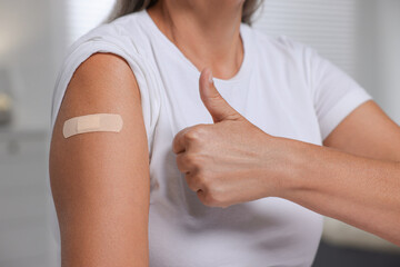 Woman with adhesive bandage on her arm after vaccination showing thumb up against blurred...
