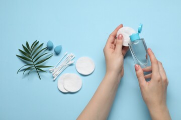 Woman using makeup remover, closeup. Sponges, cotton pads and buds on light blue background, top...