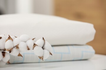 Fototapeta na wymiar Bed sheets and cotton branch with fluffy flowers on white table indoors, closeup