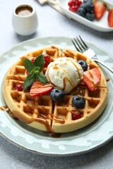 Delicious Belgian waffles with ice cream, berries and caramel sauce served on grey table, closeup