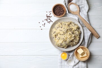 Chocolate chip cookie dough in bowl and ingredients on white wooden table, flat lay. Space for text