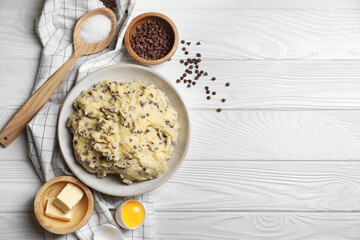 Chocolate chip cookie dough in bowl and ingredients on white wooden table, flat lay. Space for text
