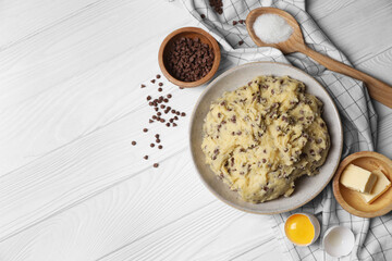 Chocolate chip cookie dough in bowl and ingredients on white wooden table, flat lay. Space for text