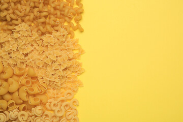Obraz premium Different types of pasta on yellow background, flat lay. Space for text
