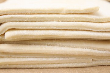 Stacked sheets of raw puff pastry dough as background, closeup