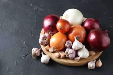 Fresh raw garlic and onions on black table. Space for text