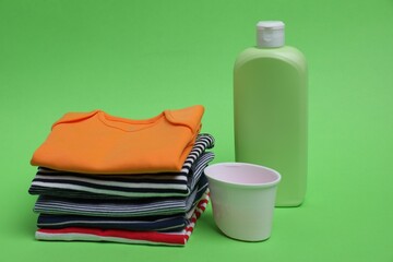 Stack of baby clothes and laundry detergents on light green background