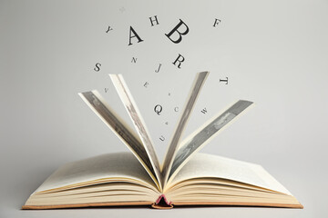 Open book with letters flying out of it on light background