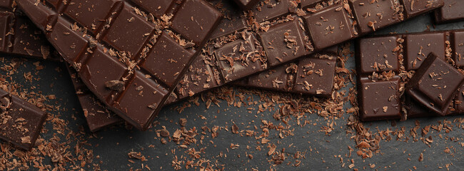 Tasty chocolate bars and shavings on dark grey table, flat lay. Banner design