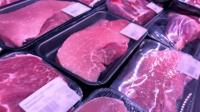 Raw pork and beef steaks in plastic containers covered with cling-wrap in a supermarket fridge. Close-up shot
