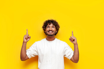 young indian guy pointing with hands up on yellow isolated background, south asian man in white...