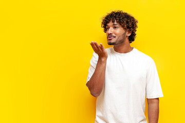 young indian guy blowing a kiss over yellow isolated background, south asian man in white t-shirt...