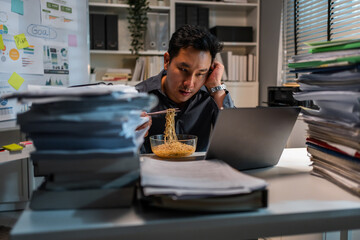 Asian young businessman eating noodles while working in office at night. 