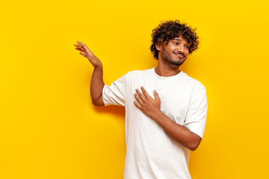 young indian carefree guy refusing and avoiding on yellow isolated background, south asian man in white t-shirt waving