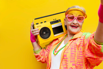 funny old granny with tape recorder in sports hipster clothes takes selfie online on yellow...