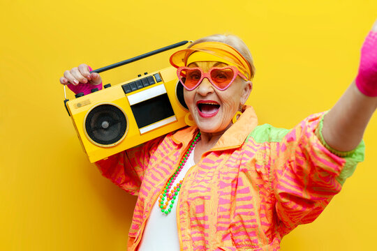 funny crazy old granny with tape recorder in sports hipster clothes listens to music and sings on yellow background