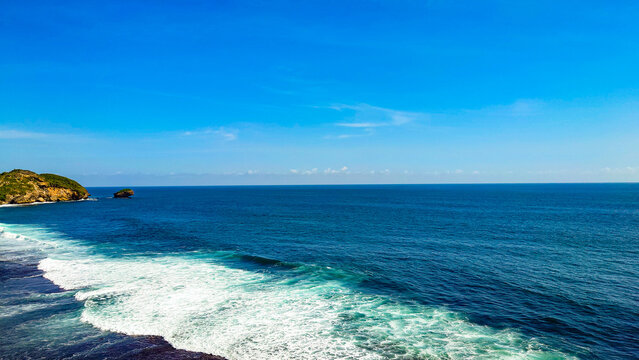 Landscape photo of the expanse of sea looks blue and the sky is clear blue and you can see rocky hills from a distance, good for a natural background