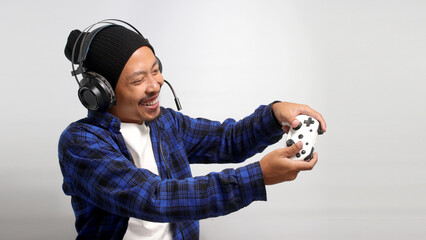 Side view of An enthusiastic Asian gamer, adorned in a beanie hat, casual shirt, and headphones,...