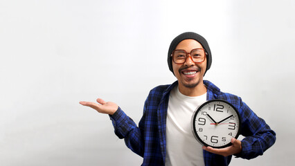 Smiling Asian man, wearing eyeglasses, a beanie hat, and a casual shirt, points or displays towards...