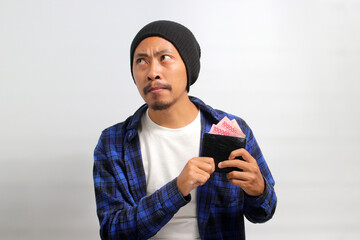 A hesitant young Asian man contemplates strategies to increase his earnings while holding a wallet...