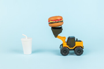 A glass with a drink and a bulldozer delivering a hamburger. © kvladimirv