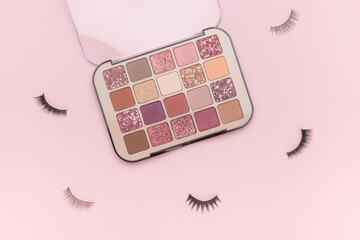 A set of eye shadow and false eyelashes on a pink background.