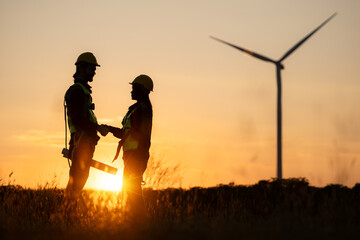 Silhouette of engineer and worker shaking hands on wind turbine background