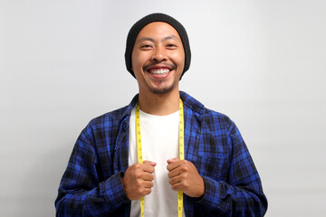 A confident young Asian man, dressed in a beanie hat and casual shirt, smiles at the camera while...