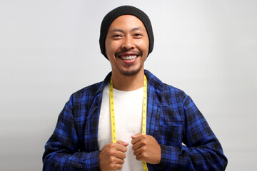 A confident young Asian man, dressed in a beanie hat and casual shirt, smiles at the camera while...
