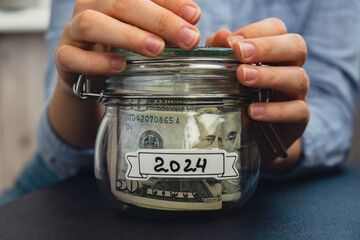 Unrecognizable woman holding Saving Money In Glass Jar filled with Dollars banknotes. 2024...