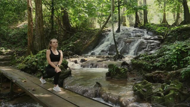 Young woman enjoys serene moment at forest waterfall. Nature and relaxation.
