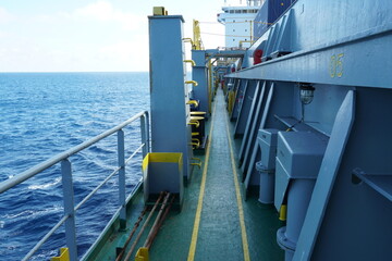 Main deck of container vessel painted green viewed from forward part of the ship. In the aft is white superstructure and on the side grey hatch coamings and railings.