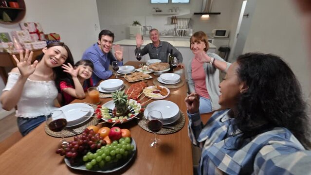 Big Family With Multi Ethnic Making Selfie Video Call Via Mobile Phone  While Eating Together Christmas Party At Home. Group Of Kinfolk Various Ages Celebrating New Year Party In Dining Room.