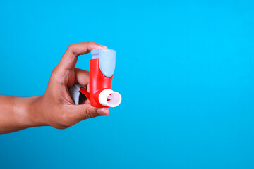 Man hand holding asthma inhaler on blue background with space for text