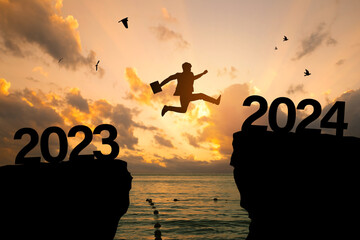 Welcome Merry Christmas and 2024 New Year concept, Silhouette of a businessman jumping on a cliff...