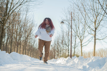 Smiling chubby redhead woman running in park in winter. 